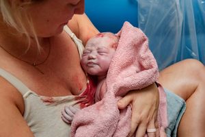 Mother holds her newborn baby wrapped in a pink towel moments after birth.