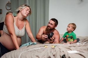 Family moment with a pregnant woman, bearded man, and toddler relaxing together on a bed at home.