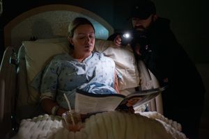 Medical professional using a flashlight to show a pregnant woman something on a tablet in a dark hospital room.