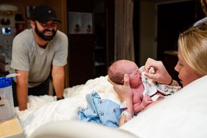 Happy father smiling as a nurse tends to his newborn baby on a hospital bed beside the mother.