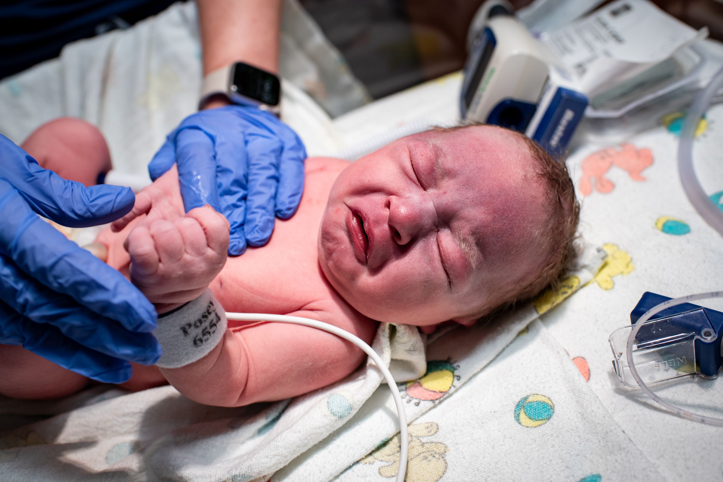 Medical professional placing ID bracelet on crying newborn baby in hospital.