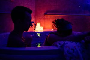 Couple sharing intimate moment in a candlelit bath with purple ambient lighting.