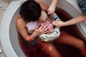 Mother cradling her newborn in a birthing tub with medical staff assisting during a water birth delivery.