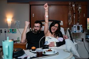 Joyful couple celebrating in a hospital room after childbirth, mother holding newborn while both cheer.