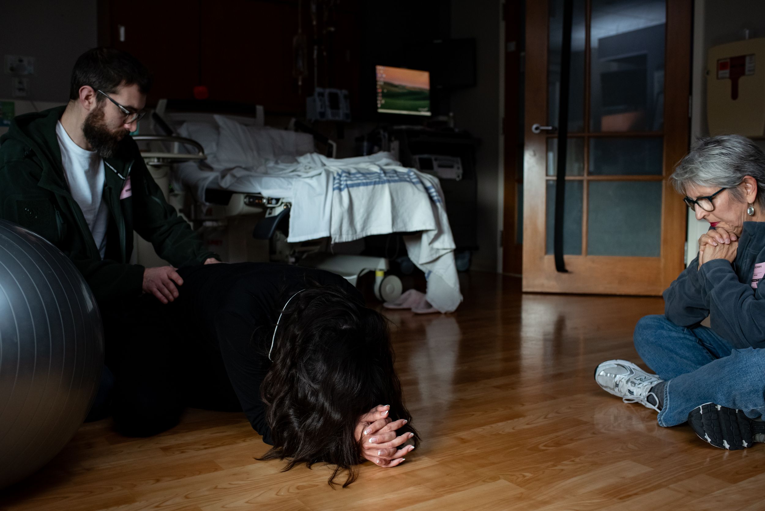 Woman in active labor kneeling on floor with support team nearby.