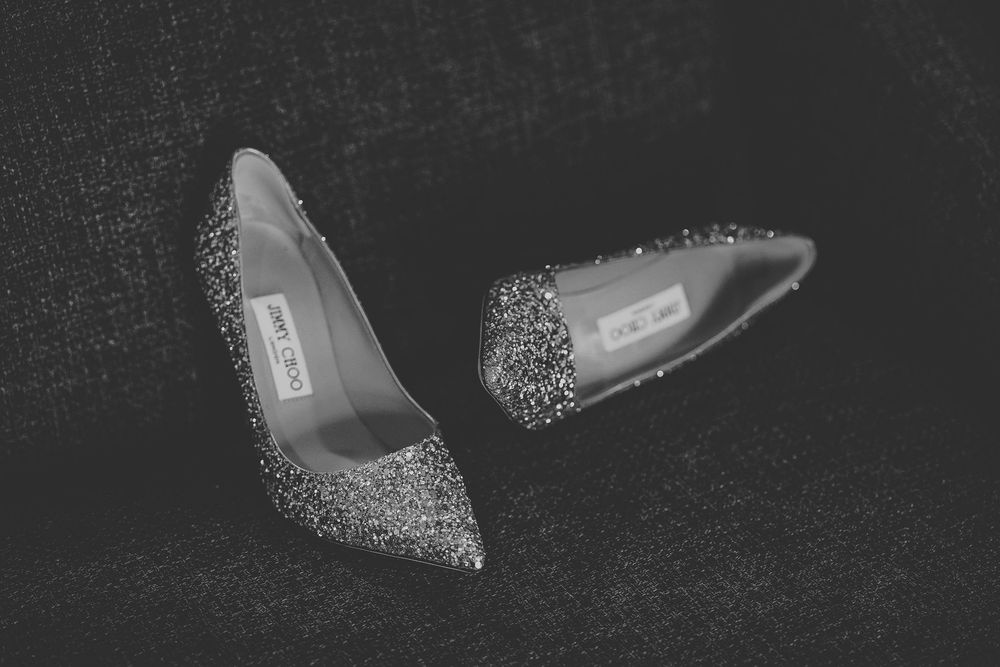 Black and white photo of sparkling glitter Jimmy Choo bridal heels on textured surface.