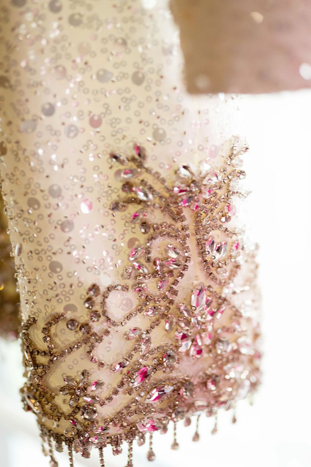 Close-up detail of elegant bridal gown with pink crystal beading and intricate embroidery.