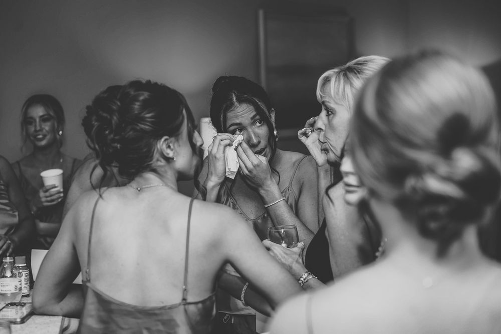 Black and white photo of bridesmaids helping emotional bride with makeup during wedding preparations.