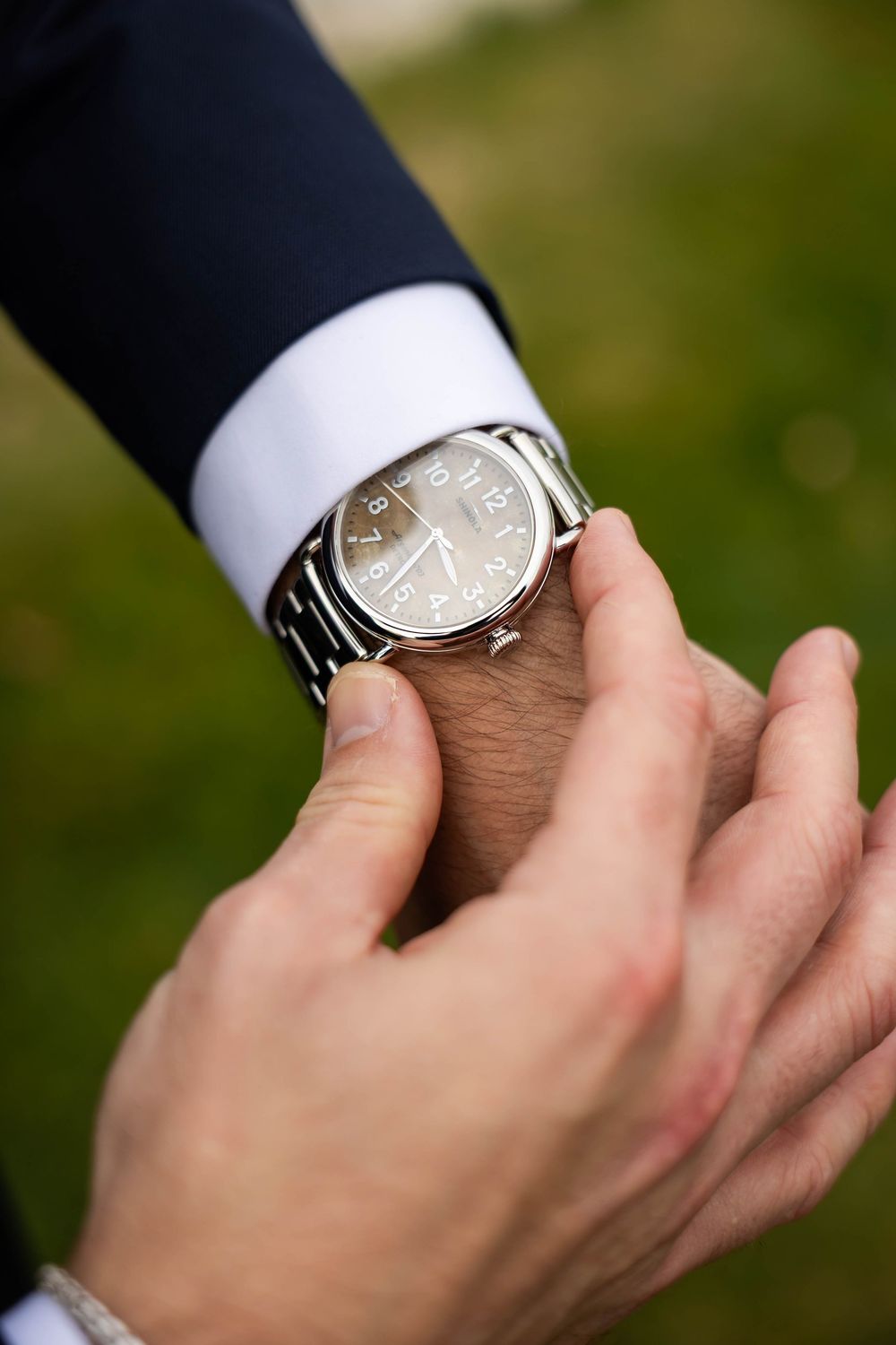 Close-up of groom adjusting silver wristwatch on suit sleeve before wedding ceremony.