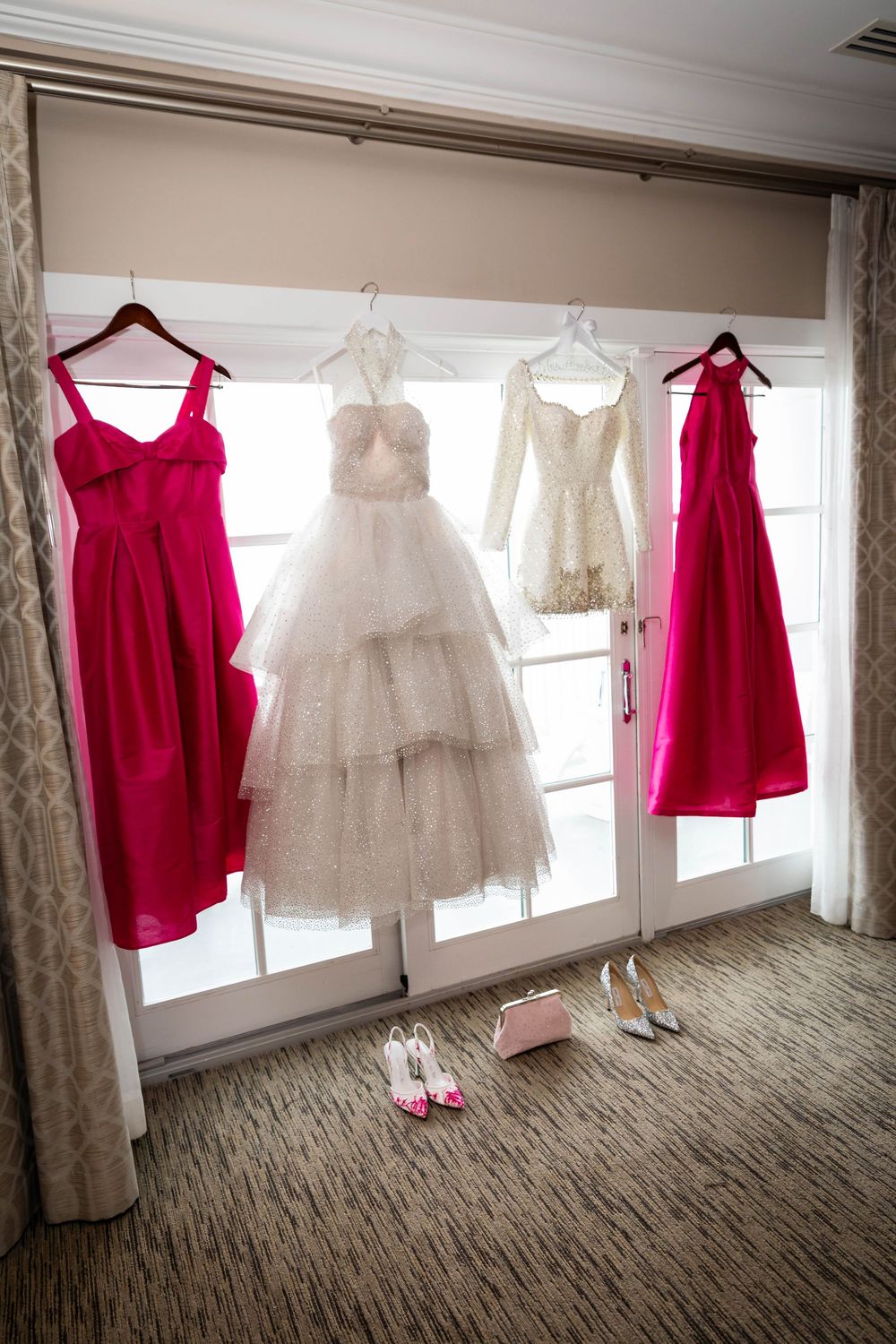 Wedding dresses and hot pink bridesmaid gowns hanging on display with bridal shoes arranged below.