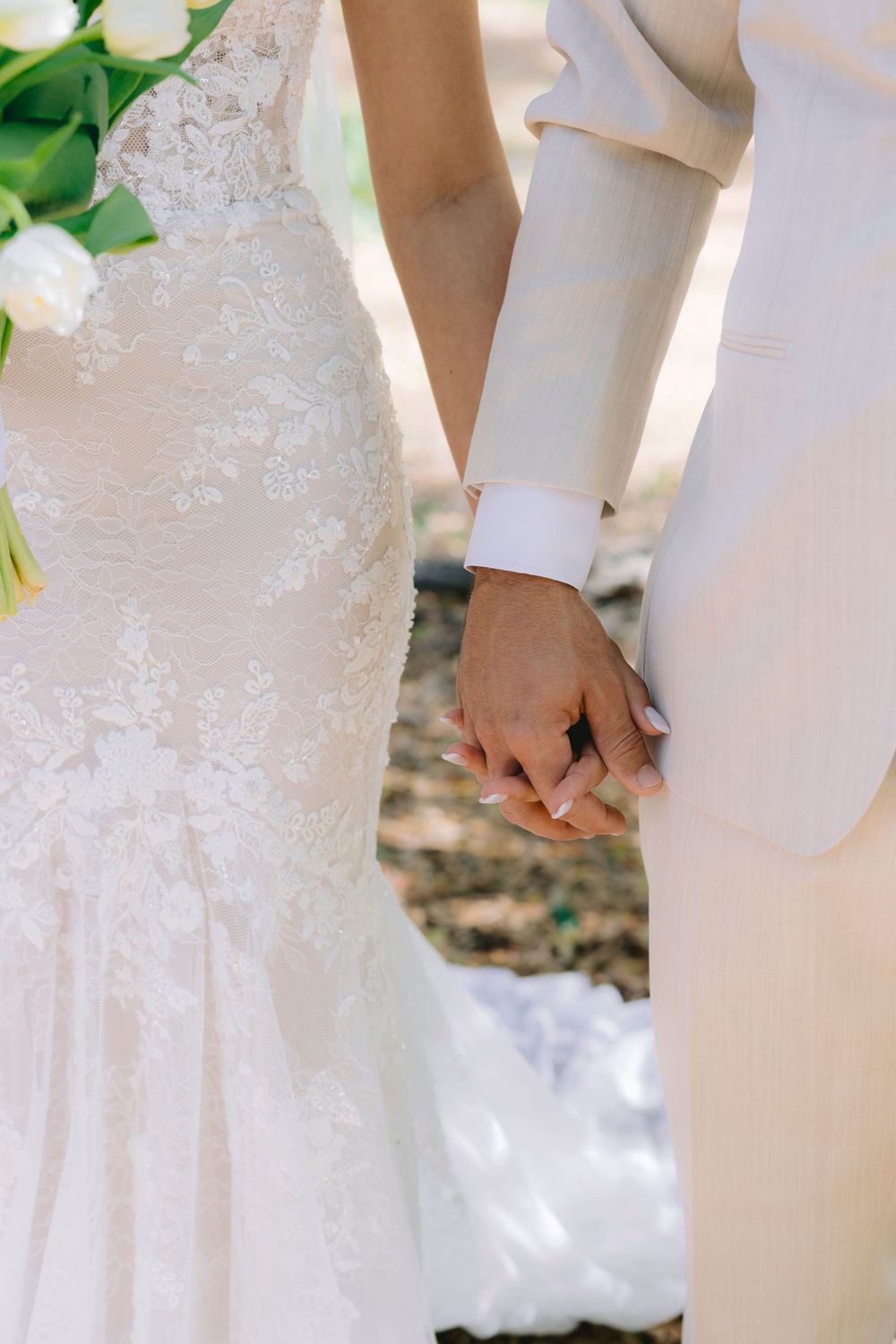Bride and groom holding hands at wedding ceremony, bride in lace gown, groom in beige suit.