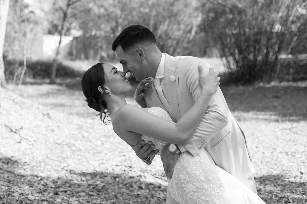 Black and white photo of a bride and groom sharing a romantic dip kiss outdoors on their wedding day.
