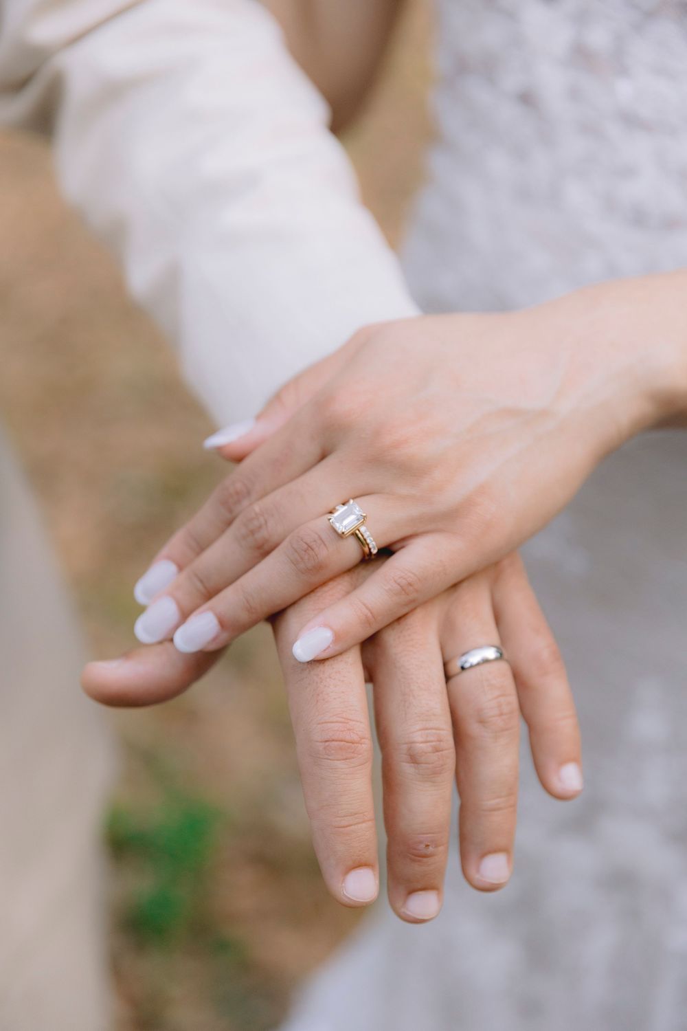 Close-up of bride and groom hands showing diamond engagement ring and gold wedding bands.