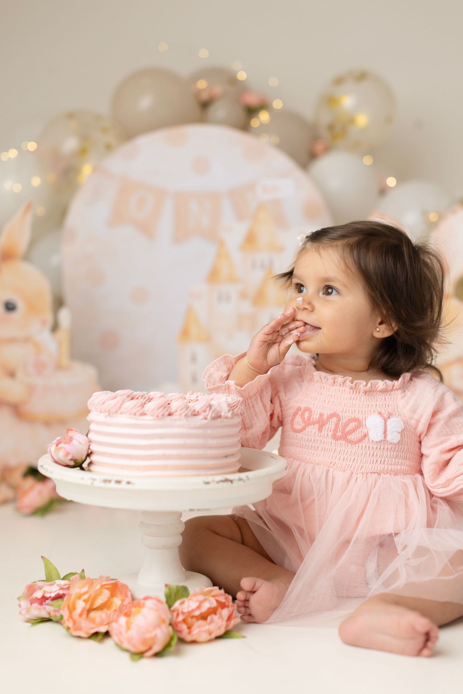 Baby girl in pink dress eating first birthday cake at cake smash photo session with floral decor. Elizabeth Lang Photography Surrey