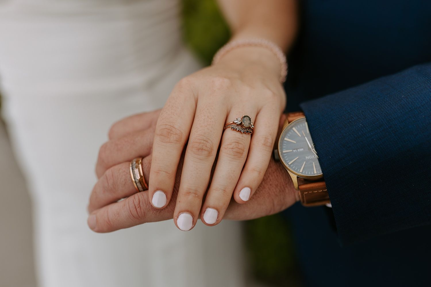 Close-up of bride and groom hands showing wedding rings and a brown leather watch on wedding day.