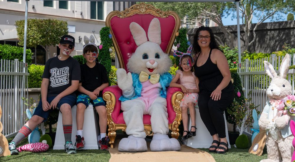 Family with two boys and girl posing with Easter Bunny character on decorative throne outdoors.