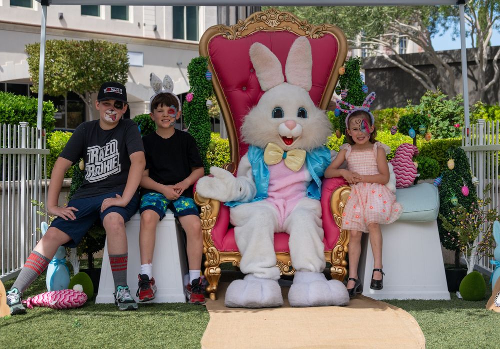 Three children sitting with Easter Bunny mascot on gold throne during Easter photo opportunity outdoors.