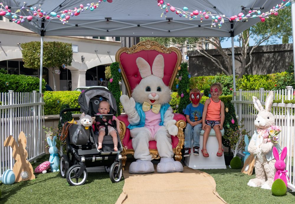 Children pose with Easter Bunny character seated on ornate pink throne at outdoor Easter celebration.