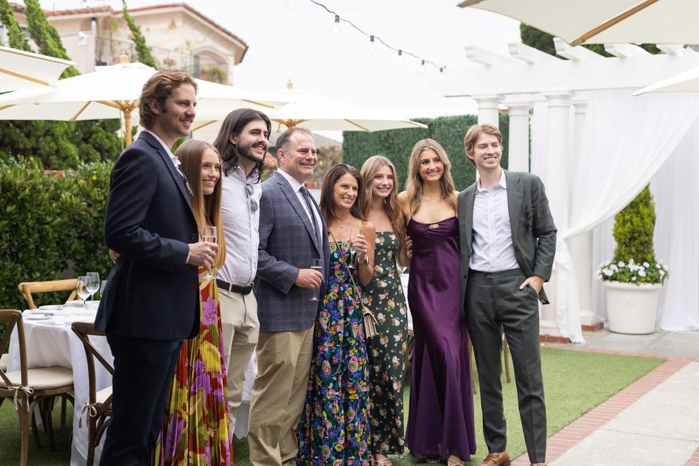 Group of seven elegantly dressed guests posing together at an outdoor wedding reception.