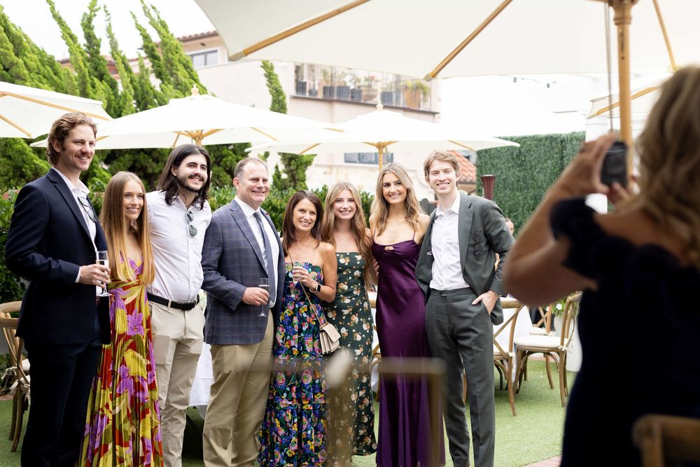 Group of wedding guests posing for a photo in a garden with white umbrellas.