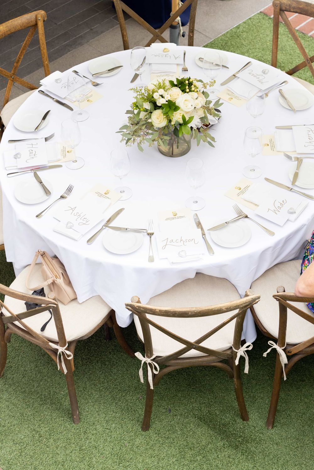 Aerial view of a round wedding reception table with white linen, floral centerpiece, and personalized place cards.