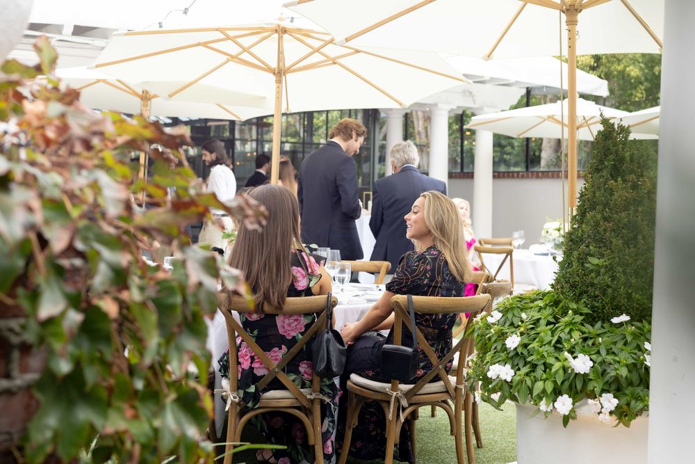 Guests dining at an elegant outdoor patio restaurant surrounded by lush greenery and white umbrellas.