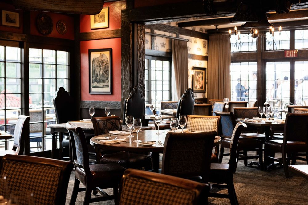 Upscale restaurant interior with dark wood furniture, red walls, vintage artwork, and elegant table settings.