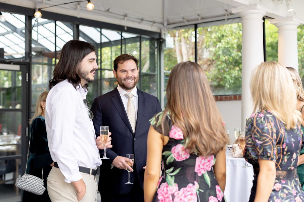 Guests mingling with champagne at elegant outdoor wedding cocktail hour under white tent pavilion.