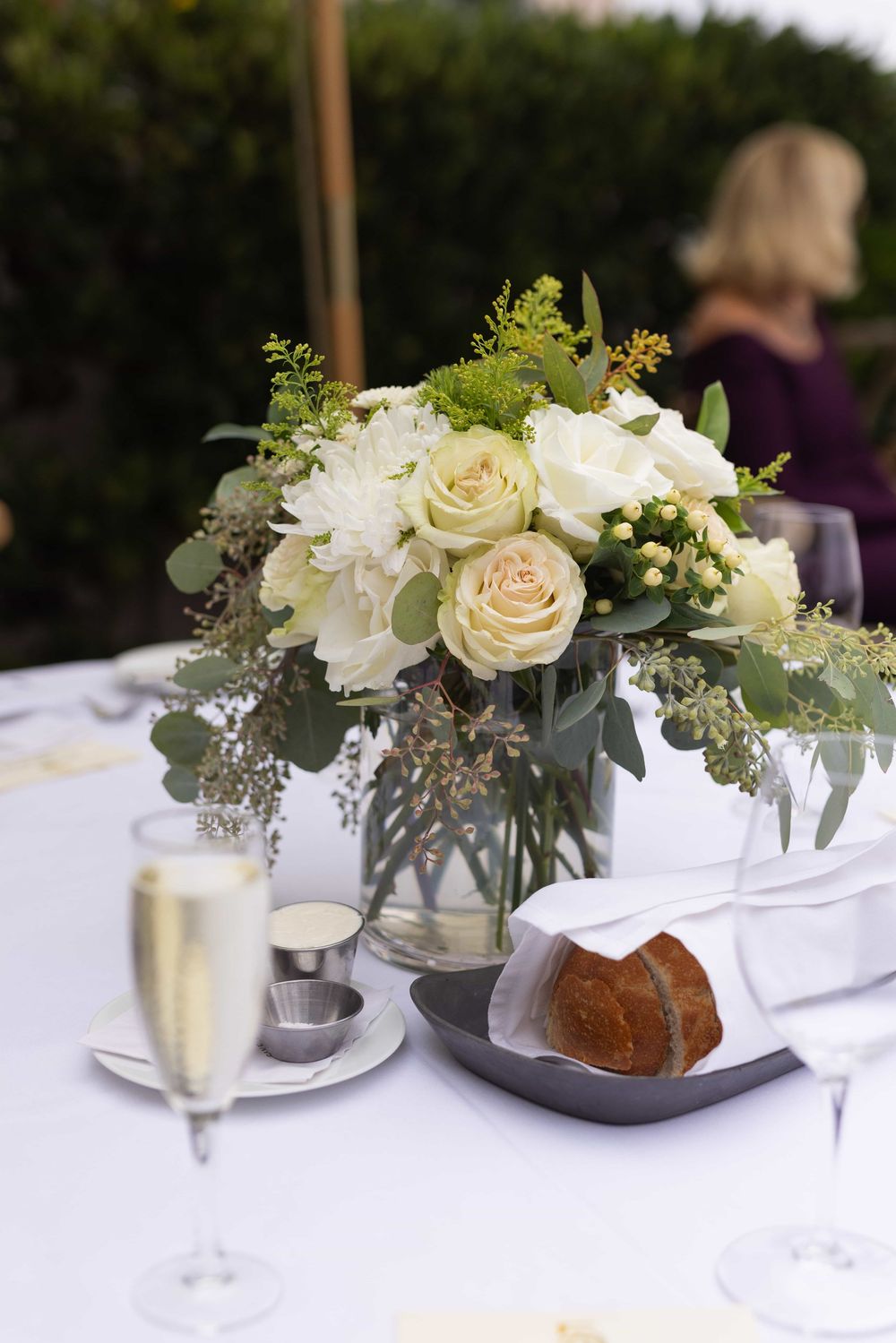 Elegant wedding table centerpiece with white roses, champagne flute, and bread roll.