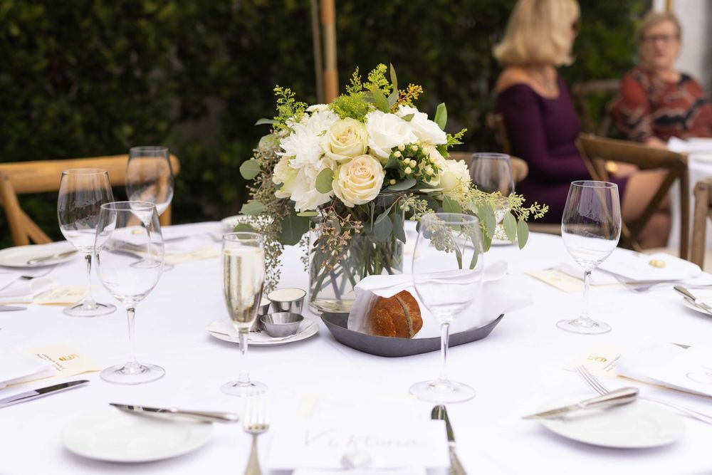 White rose centerpiece on a formal outdoor wedding reception table with place settings.