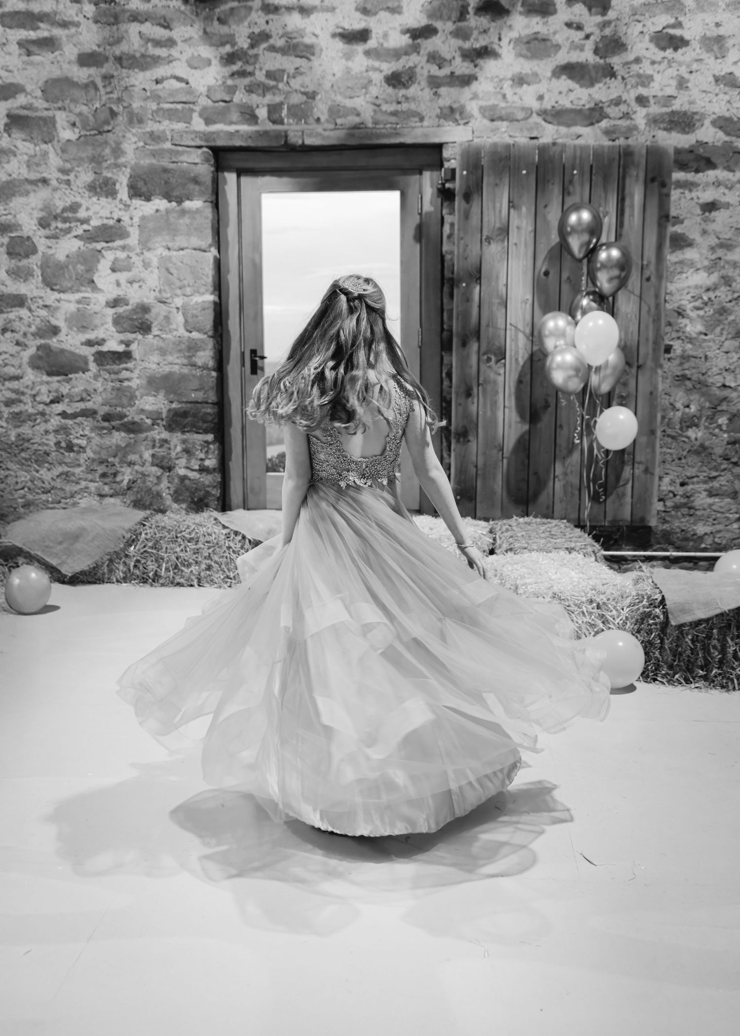 Black and white photo of a woman in a flowing gown twirling on a dance floor in a rustic stone venue.