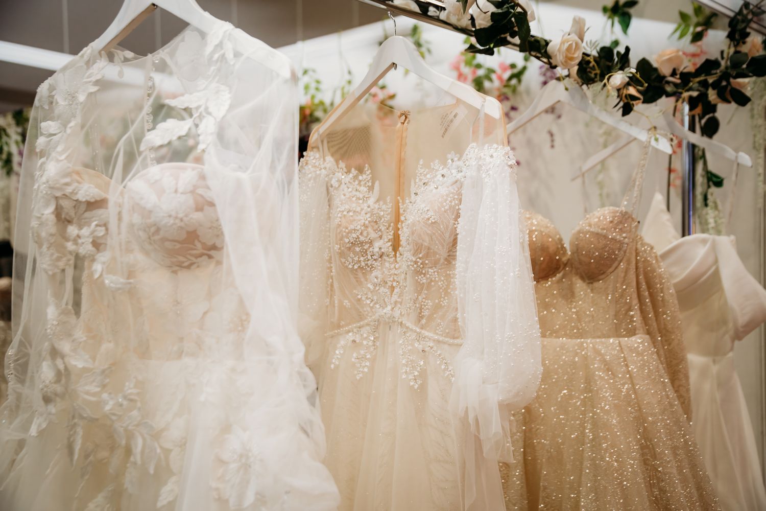 Elegant white and champagne beaded wedding gowns displayed on hangers in a bridal boutique.