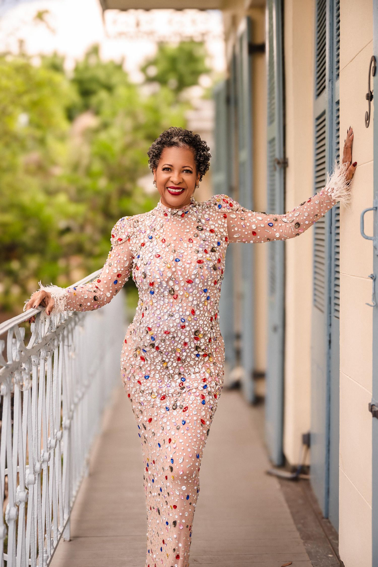 A person in a floral print dress poses playfully along a balcony railing with blue shutters. confident boudoir poses for women