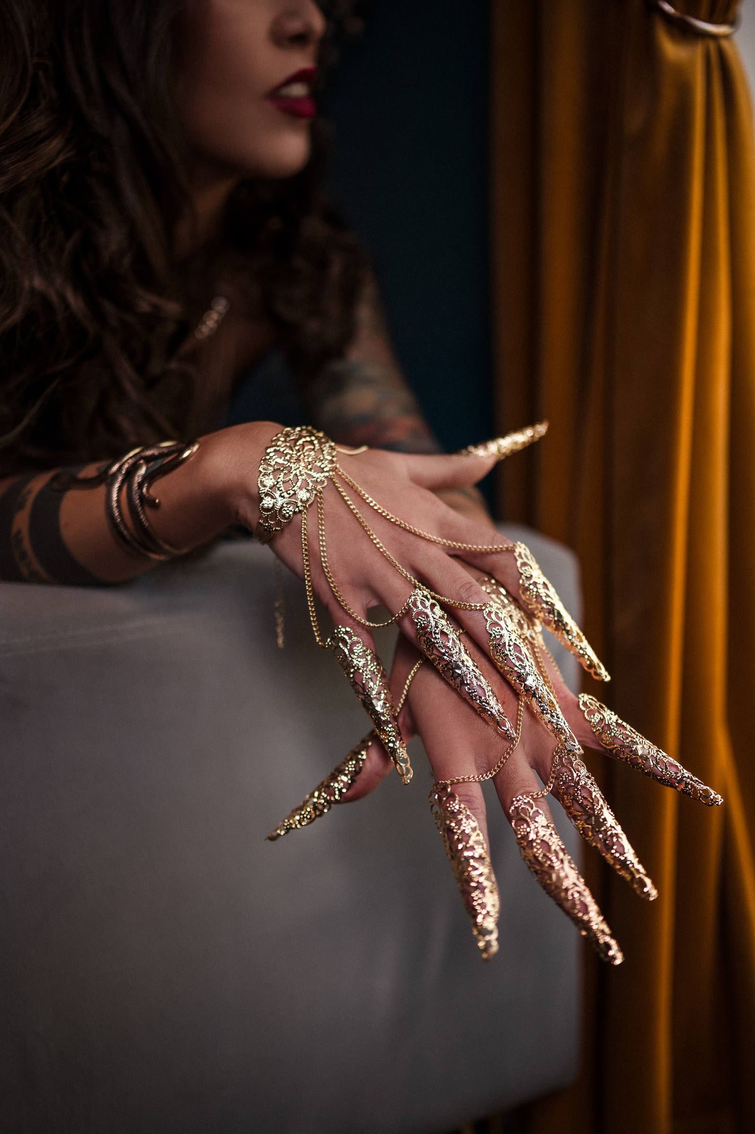 Ornate gold nail extensions and jewelry adorning hands against dark background with gold curtains. playful boudoir photography
