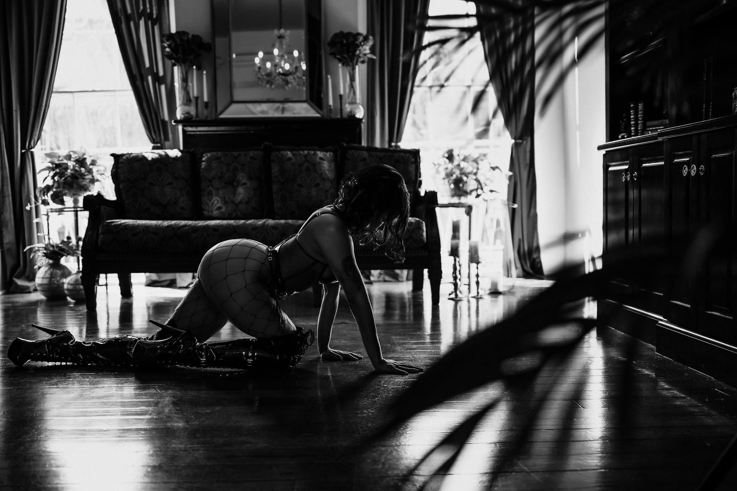 Dramatic black and white silhouette of a dancer stretching on hardwood floor with piano and window shadows. flirty boudoir photography