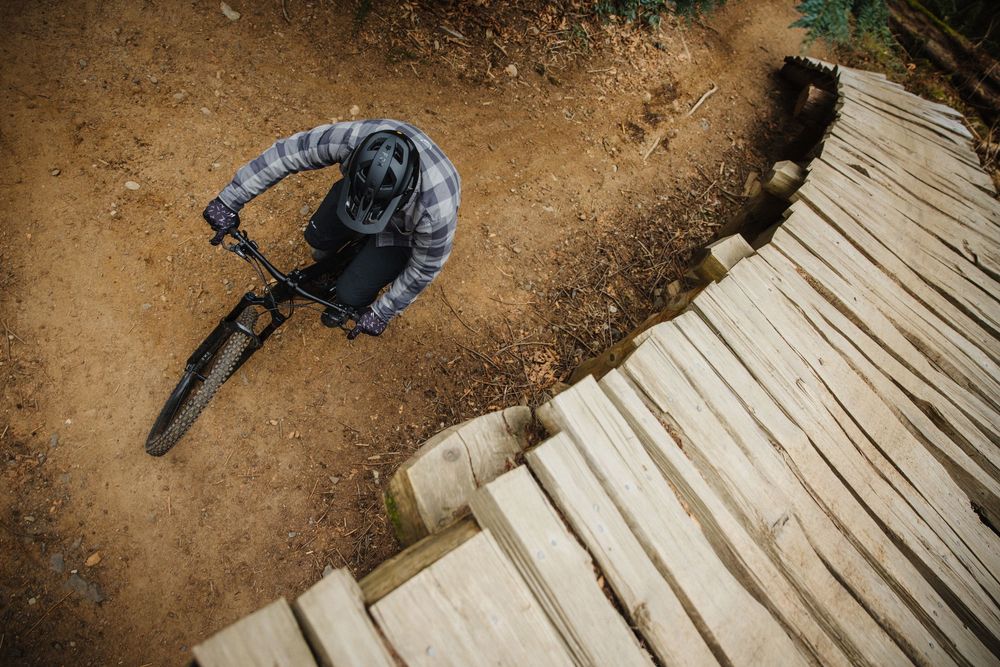 Aerial view of a mountain biker riding a wooden berm on a dirt trail.