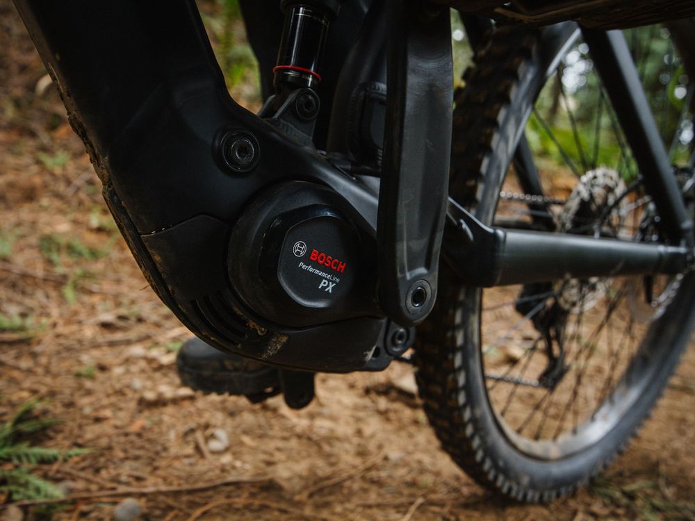 Close-up of a Bosch Performance CX mid-drive electric bike motor mounted on a mountain e-bike frame on dirt trail.