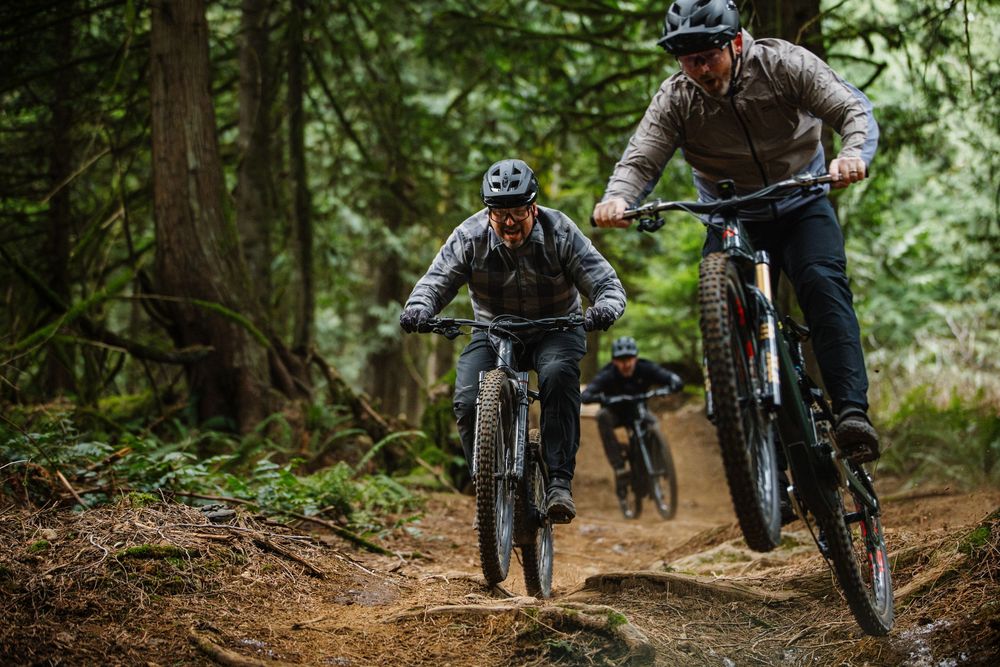 Three mountain bikers riding through a lush forest trail on rugged mountain bikes.