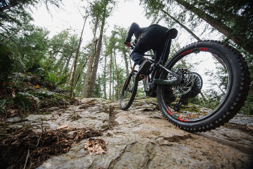 Mountain biker riding over rocky terrain in a misty forest on a full-suspension trail bike.