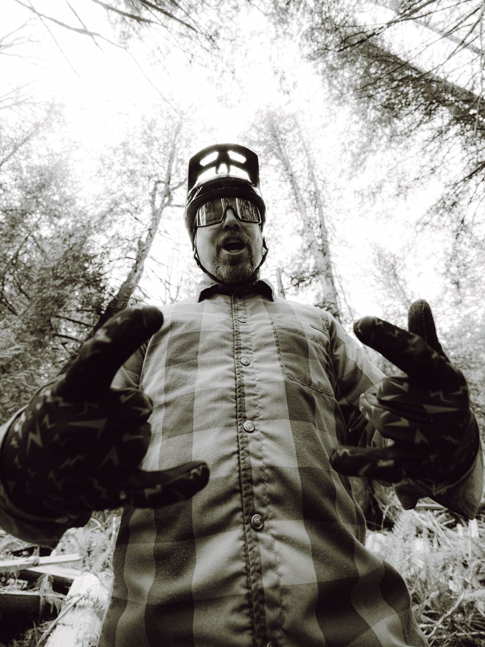Mountain biker in plaid shirt and helmet gear posing in forest, black and white photo.