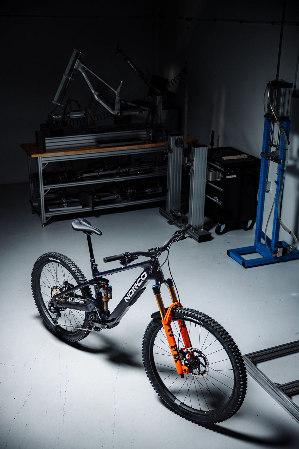 Norco mountain bike with orange forks displayed in a dark workshop garage setting.