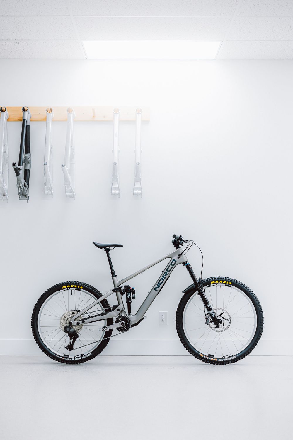 A gray Norco mountain bike leans against a white wall in a clean modern bike workshop.