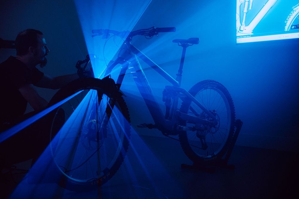 Silhouette of a mountain bike displayed under dramatic blue lighting with a projected image in background.