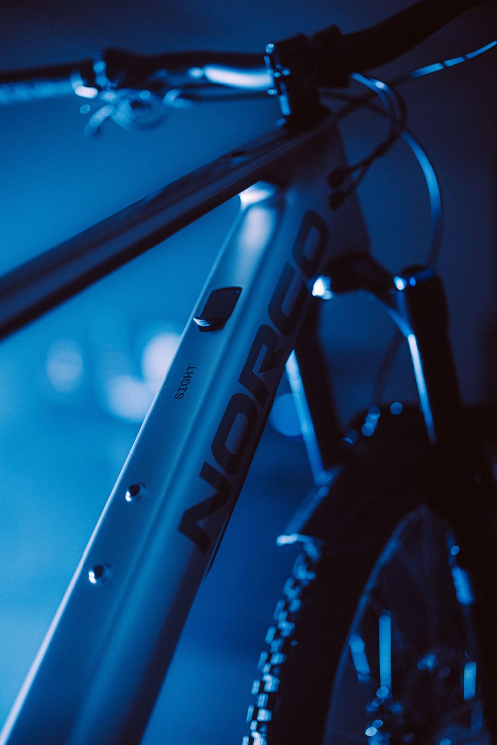 Close-up of a Norco mountain bike frame in dramatic blue lighting, showcasing sleek design and premium build quality.
