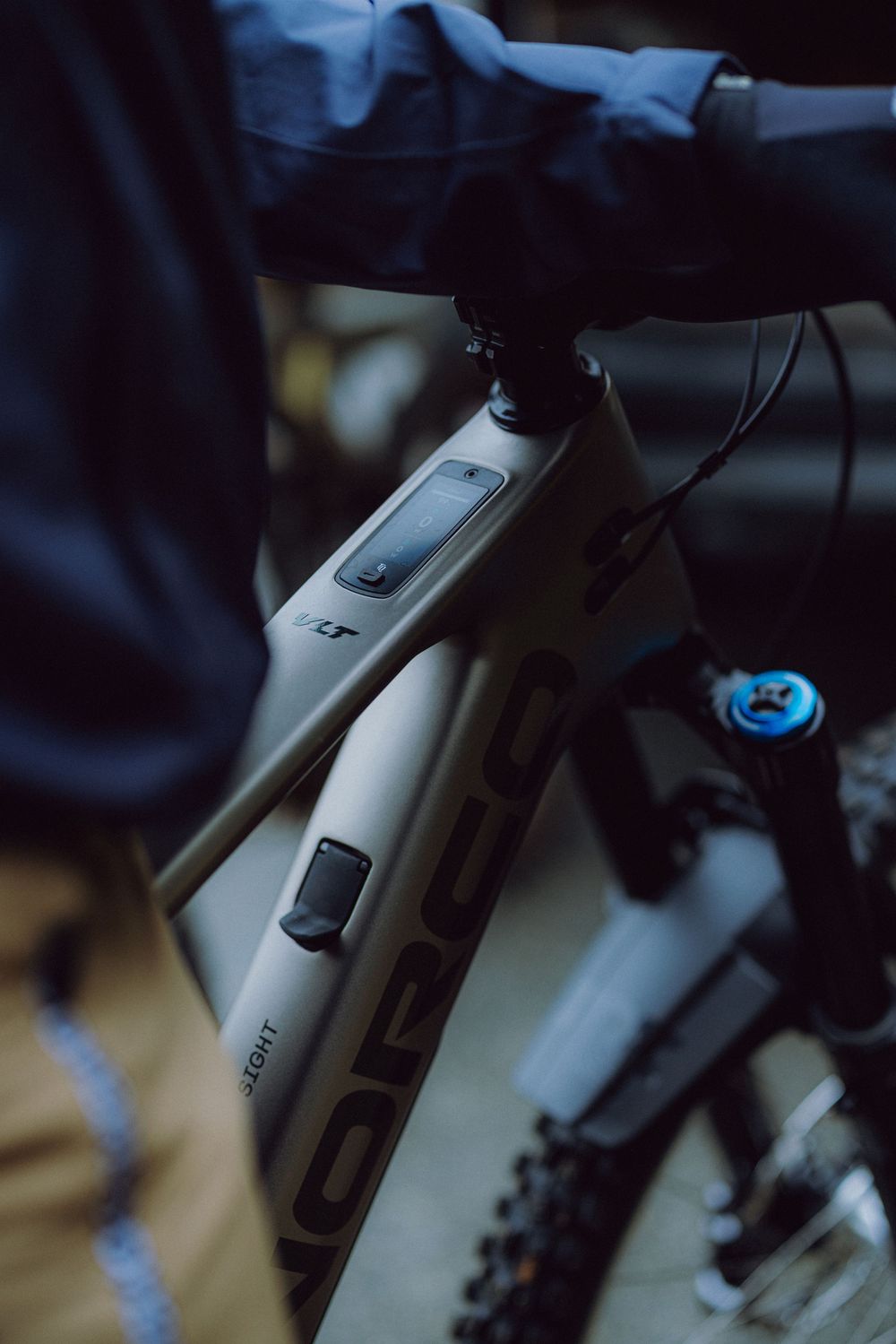 Person in jacket inspecting a Norco LT mountain bike frame with visible power button and cable routing.