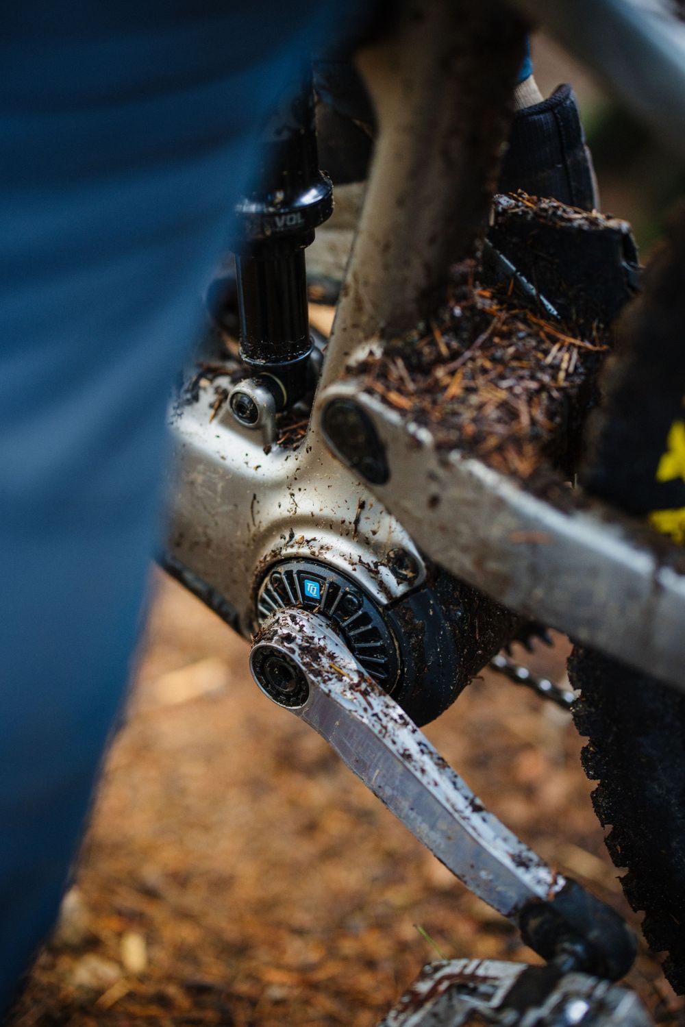 Close-up of a muddy mountain bike bottom bracket and crank arm covered in dirt after an off-road trail ride.