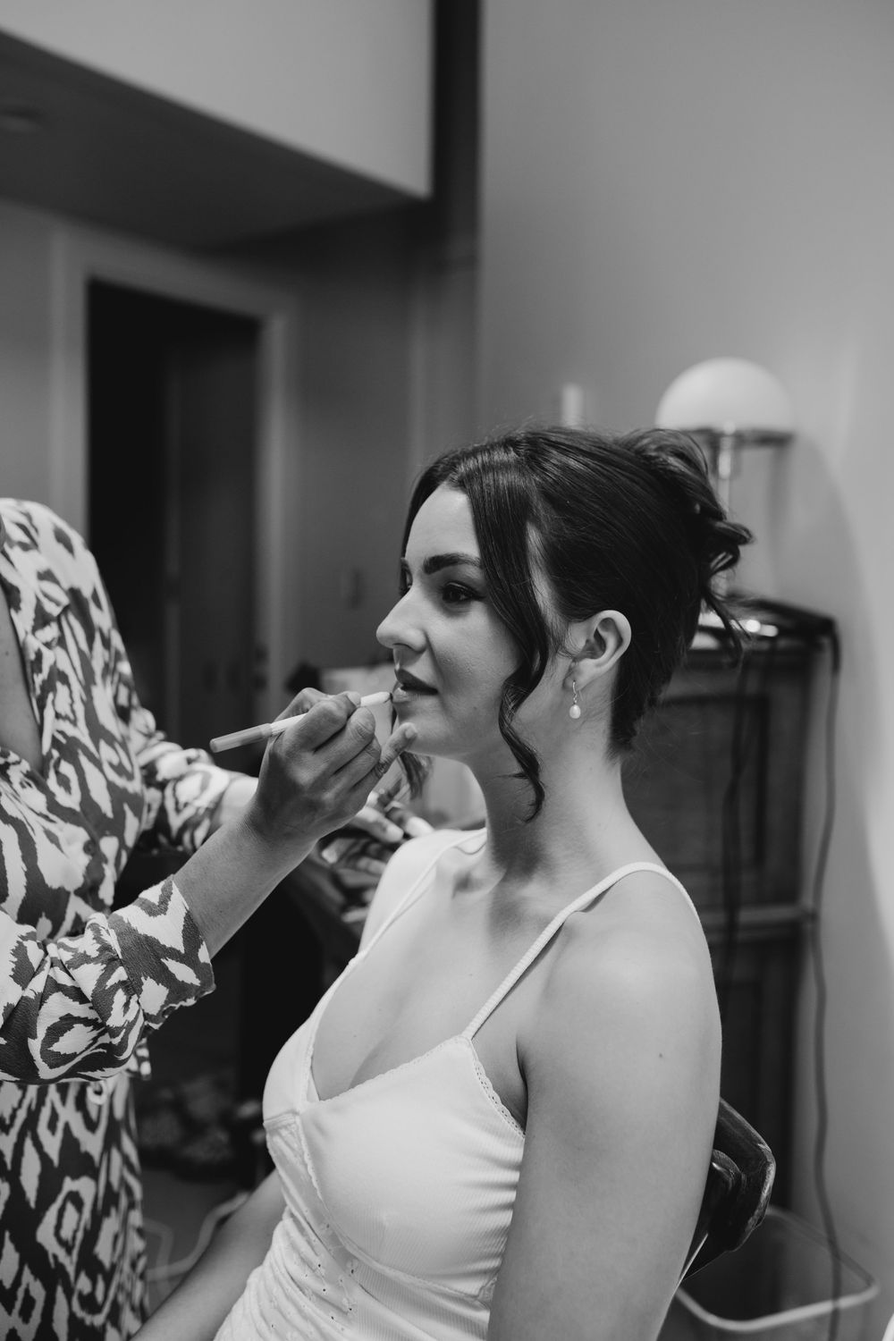 Bride having makeup applied by artist while smiling in black and white getting ready photo.