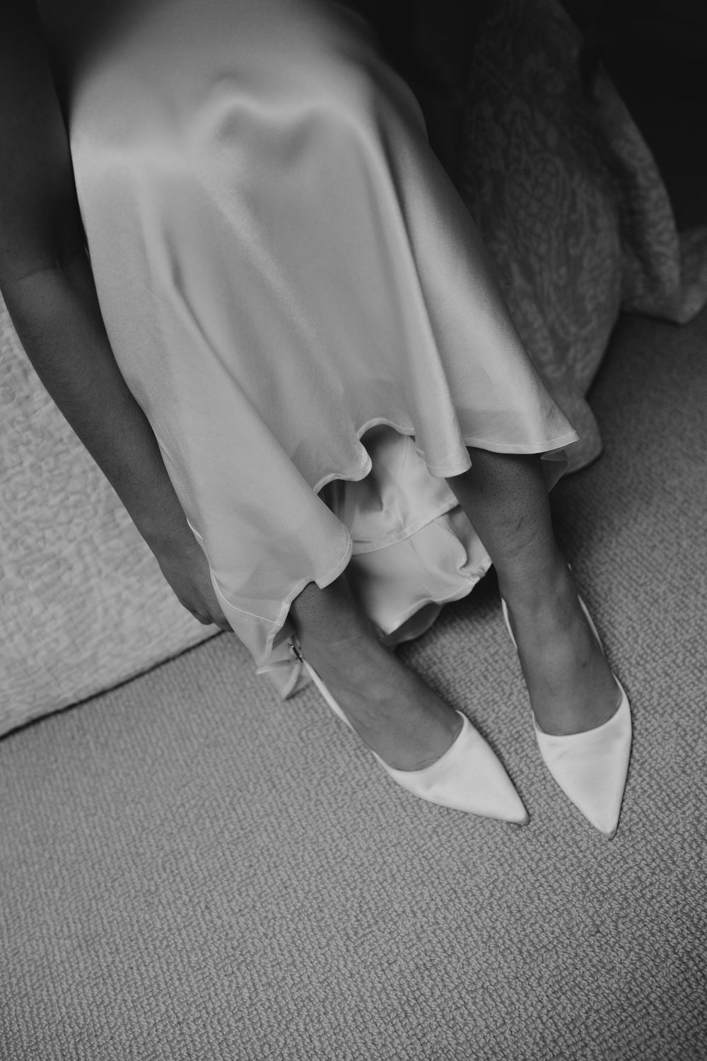 Close-up of bride wearing white pointed-toe heels with flowing satin wedding dress hem.