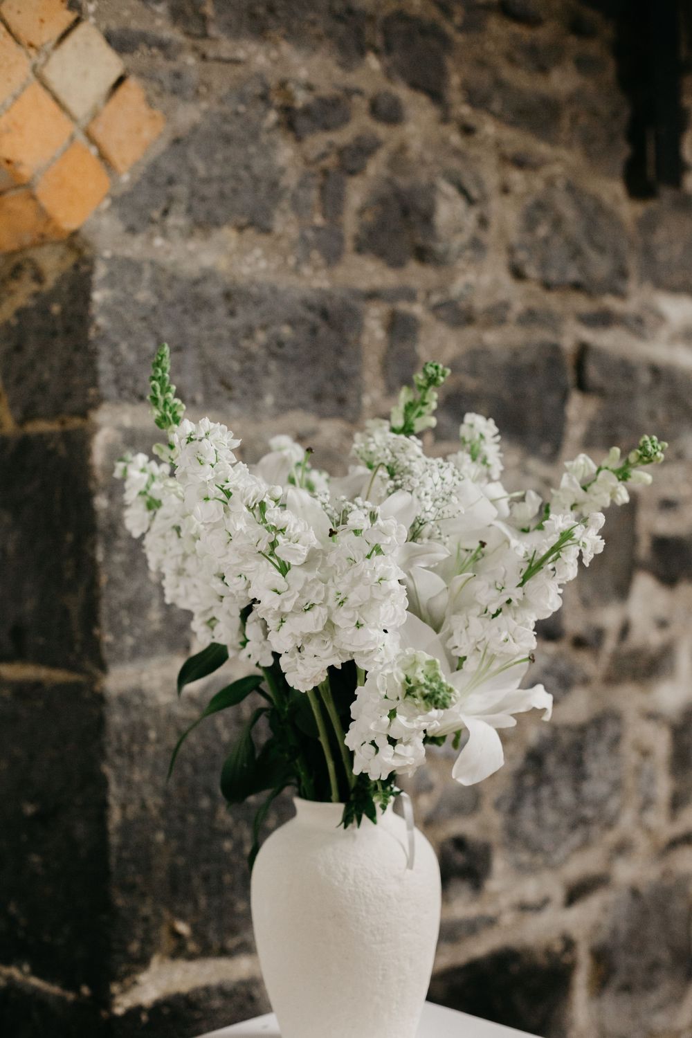 White floral wedding arrangement with lilies and stock flowers in white ceramic vase.