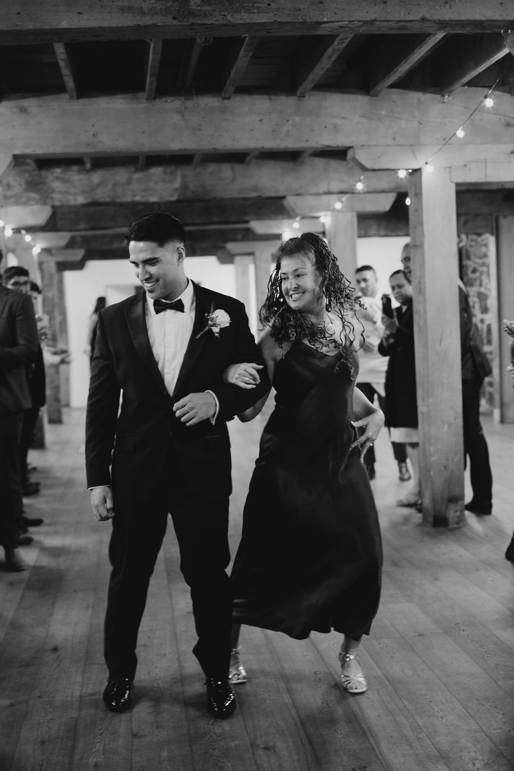 Couple dancing joyfully at wedding reception in rustic barn venue with string lights.
